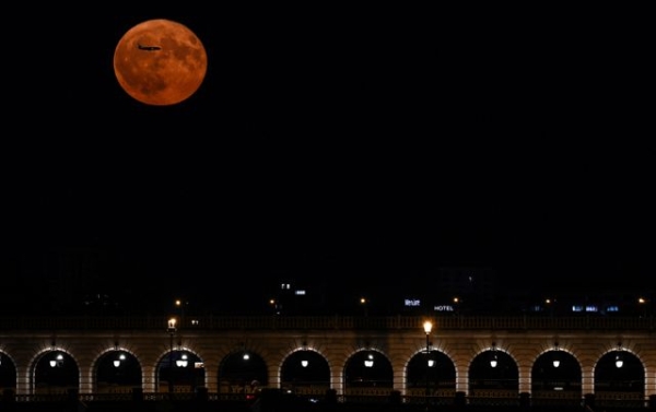 A plane seen flying across the Buck Moon in the sky above Paris