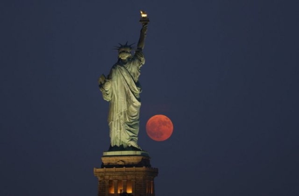 A 99.7 percent illuminated Buck Moon rises through a haze behind the Statue of Liberty in New York City on July 2, 2023