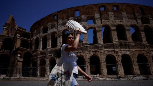 A woman uses a fan to shelter from the sun during a heatwave in Italy. The Colosseum is visible in the background.