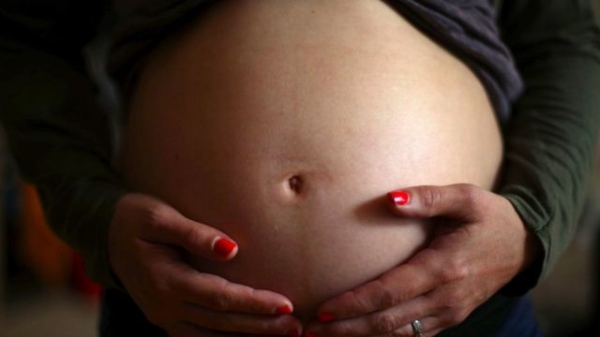 A pregnant woman rests her hands on her stomach