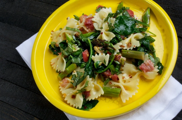Тарілка з пастою, беконом та зеленню на жовтій тарілці